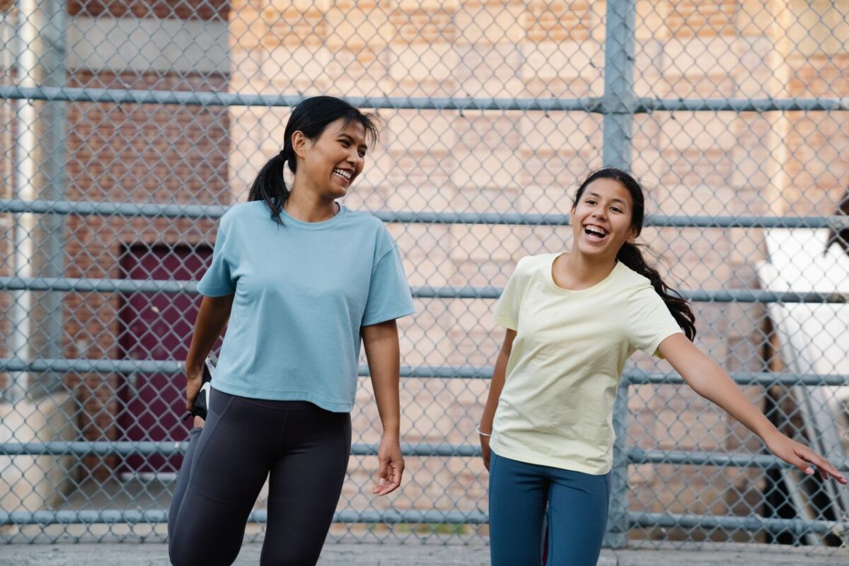 Two women laughing together outdoors, wearing casual T-shirts, joyful moment. Urban setting.